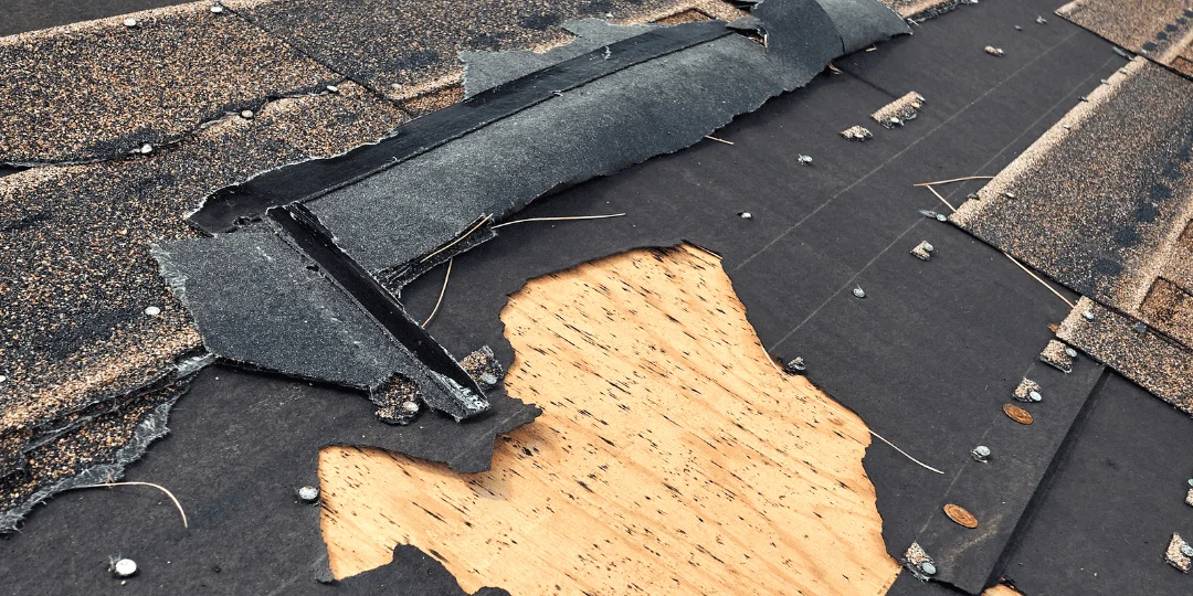 Wind-damaged asphalt roof with shingles torn away, exposing underlayment and bare decking